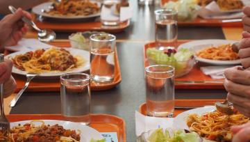 Photo d'une table de cantine avec plateaux remplis et mains d'enfants en train de manger